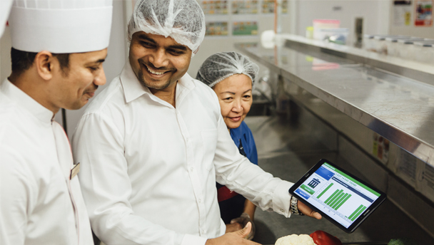 A Sodexo chef is showing food waste management app on a tablet to his colleagues
